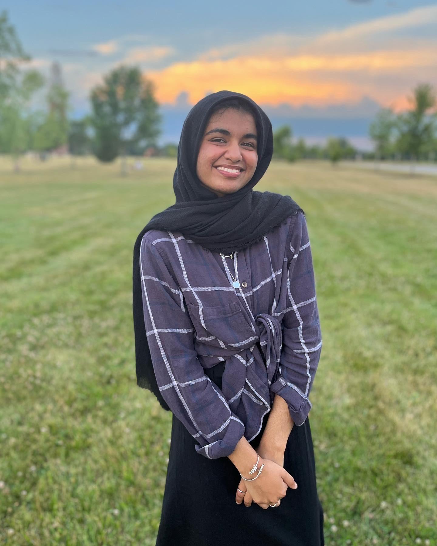 A female student stands outside in a field smiling